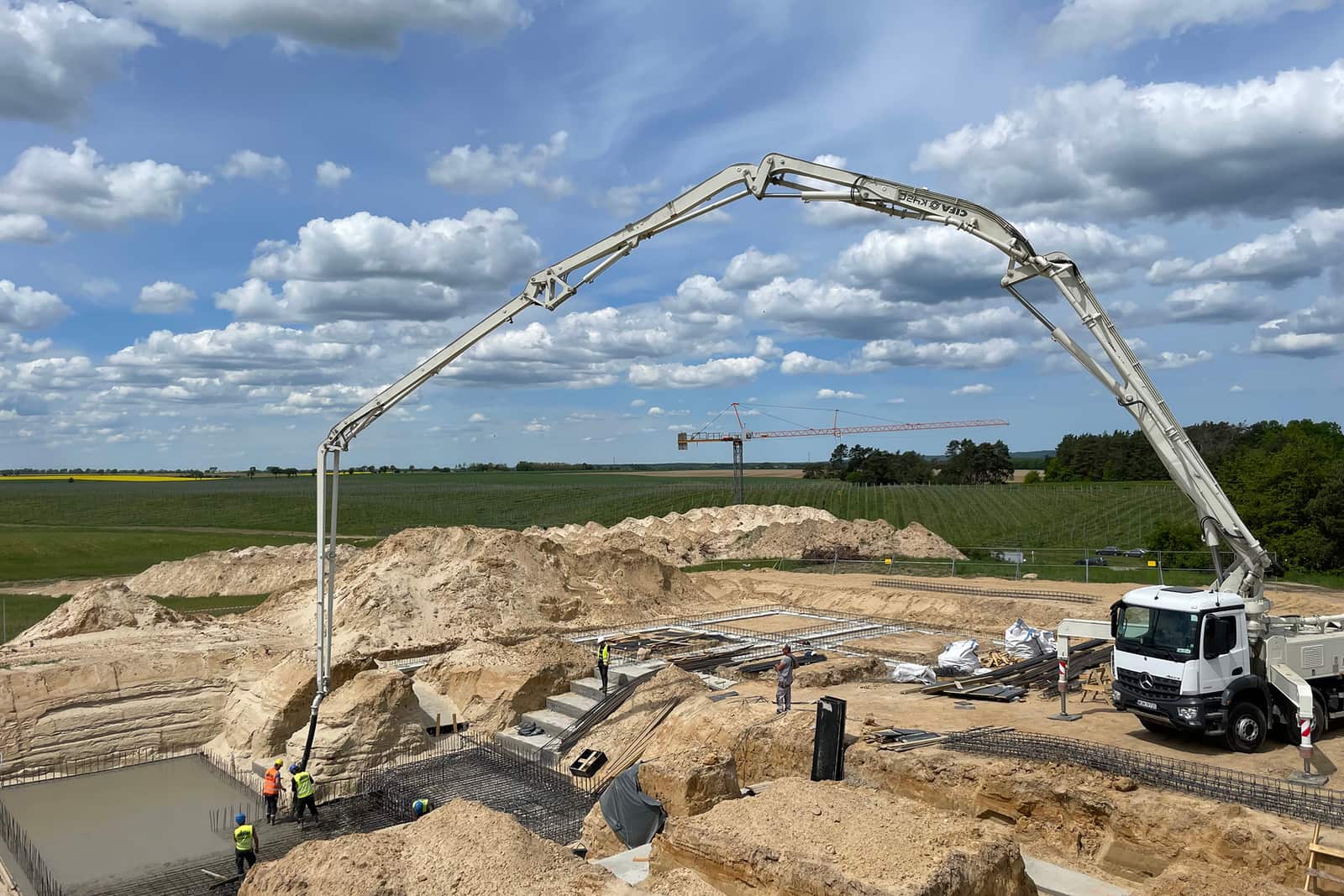 Pompa do betonu nad wykopem z fundamentami, ekipa przy zbrojeniu