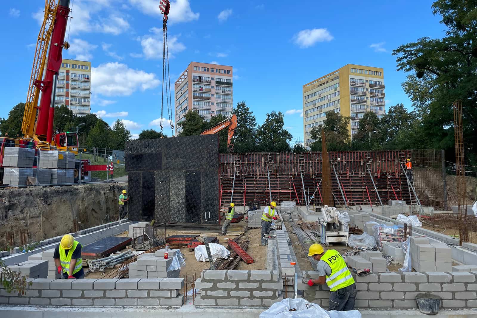 Ekipa PDM Construction przy ścianach fundamentowych, w tle żuraw i szalunki